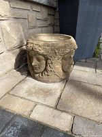 Side view of concrete planter showing two sculpted faces and rounded form on stone patio.