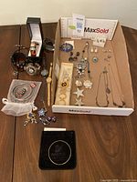 Full lot of costume jewelry arranged on a table including watches, brooches, necklaces, earrings, and Swarovski bangle in pouch.