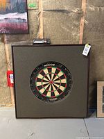 Dart board set up showing dark wood frame and grey foam surround against unfinished wall.