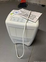 White Whirlpool dehumidifier, showing front with air vents and power cord laid out on floor.