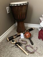 Full view of drum sitting on carpet with other percussion instruments: rain stick, maracas, shaker, and jingle bells.