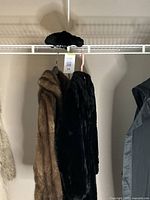 Two fur coats, brown and black, hanging on a rack with matching hats on top