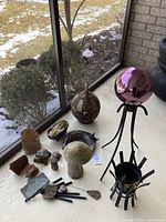 Photo of all garden decorative items assembled on a concrete floor near window showing gazing ball on black metal stand, urn, mushroom figurine, turtle, and other ceramic pieces.