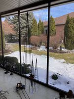Garden obelisk standing against window with snow-covered backyard visible, metal rods and pointed finial visible