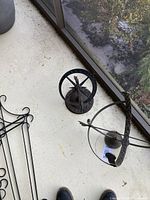 Two metal garden sundials placed side by side on a floor with a window and outdoor view in background.