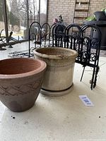 Two glazed terra cotta pots with metal garden barriers behind on porch floor.