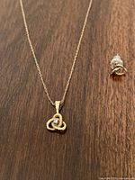 Close-up of gold chain with looped trillium pendant and single stud earring on wood surface