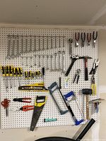 Wall-mounted pegboard displaying various hand tools including wrenches, pliers, screwdrivers, hammers, and saws organized by type and size.
