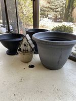 Photo showing three black resin planters of different sizes and one small wooden birdhouse in a planter on a porch area.
