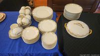 Overall view of stacks of plates, cups and covered serving pieces on blue and black cloth.