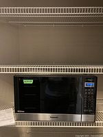 Front view of Panasonic microwave oven placed on a wire rack with paper manual beside it. Digital display shows time 10:42 and control panel buttons visible.