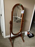 Full view of the wooden oval tilting mirror on stand against a wall on carpeted floor.