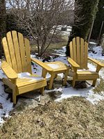 Front view of two yellow Adirondack chairs and small side table on grass with light snow