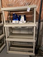 Full view of one beige plastic collapsing storage shelf unit with four slatted shelves. Two humidifiers rest on top shelf (not included).