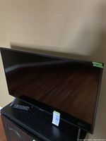 Front view of Samsung TV on stand with remote placed on furniture below; green tape marking ‘40"’ on bezel