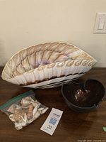 Photo showing the large ceramic shell-shaped bowl, small black bowl, and bag of shells together on a table.