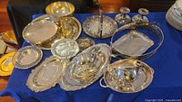 Wide view showing the full silver plate collection including trays, bowl, sauce boats, and candlesticks on a blue cloth