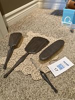 Overview of all four items arranged on a crocheted doily: hand mirror, clothes brush, hair brush, nail file