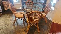 Four rattan chairs arranged around round glass-topped rattan table on tile floor