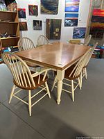 Front angle view of the dining table with six matching chairs; shows light wood top and white legs with turned details; chairs with white spindles and brown wooden seats.