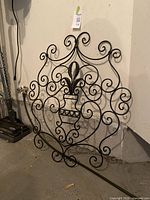 Full view of black wrought iron outdoor wall art showing entire square ornamental piece with scroll details and central vase motif.
