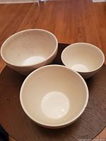 Three white cookware bowls arranged on a wooden surface showing their size difference and design.