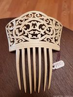 Front view of an antique carved hair comb with pierced floral and scroll design, placed on a wooden surface, showing its full length and decorative upper section.