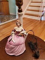 Antique porcelain lamp base figurine of a woman in a pink gown holding a fan and letter, lamp hardware attached with electrical cord.