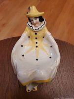 Front view of the porcelain lady jester boudoir puff dish showing painted yellow hat and dress with black buttons and details.