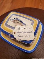 Top view of the lid of the Art Deco hand painted cheese dish with a string tag attached describing the item.