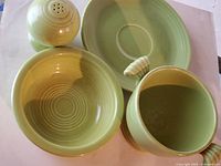 Four assorted Fiesta pieces in chartreuse green on white background. Items are salt shaker, small bowl, vase, and plate with shell handle.