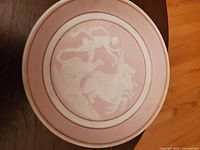 Top view of Camille Tharaud Limoges porcelain plate with white relief design of Phaeton riding horses on pink background with gold trim