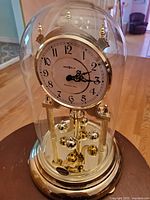 Gold-tone Howard Miller quartz clock with Westminster chime, under glass dome on a table.