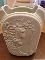 Front and back embossed female profile with floral design on white bisque vase.