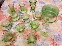 Photo showing a variety of 24 green depression glass pieces including small bowls, plates, saucers, cups, and a tall glass.