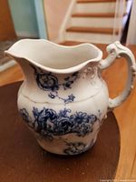 Side view of white porcelain creamer pitcher with blue floral and scroll designs, showing shape and handle detail.