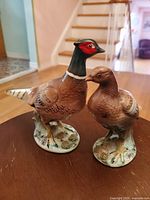 Photo of the two Japanese porcelain bird figurines on a table in a home setting showing size, colors, and details.