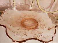 Pink depression glass bowl with scalloped edges and embossed leaf pattern on a pink background.