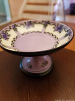 Top view showing the ceramic cake stand pedestal with pale lavender center and floral cream border with purple flowers and green leaves.