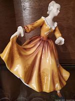 Front view of Royal Doulton Kirsty figurine in yellow-orange dress holding skirt edges.