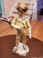 Front view of Royal Worcester figurine of a young boy in yellow outfit holding a parakeet on his arm, showing detailed craftsmanship and colors.