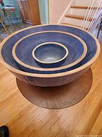 View of three nested blue ceramic mixing bowls on wooden floor with beige trim and visible age wear