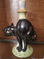 Front view showing black cat with red eyes, arched back, on pale green base