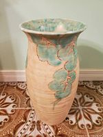Front and side view of tall ceramic vase with beige color and green-blue leaf design.