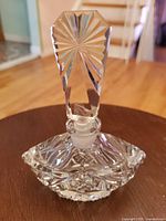 Close-up photo of the crystal perfume bottle assembled, showing the detailed faceted stopper and intricate cut glass base on a wooden surface.