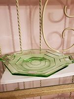 Green depression glass serving plate shown from side angle on shelf with visible octagonal shape and square handles.