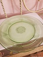 Top view of the round green depression glass platter showing embossed floral and geometric patterns near the center and edges.
