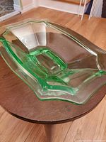 Angled oval view showing the scalloped, geometric design and green tint of the pressed glass serving bowl, placed on a wooden round table.