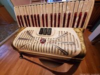 Front view of vintage Rivoli accordion showing pearlized white and red keys, three black switches, decorative grille with silver crossed lines and red 'R' emblem.