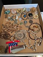 Overview of jewelry lot showing brooches, pendants and necklaces laid on cardboard background.